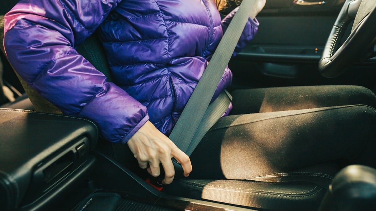 겨울용 외투를 입고 안전벨트를 매는 운전자